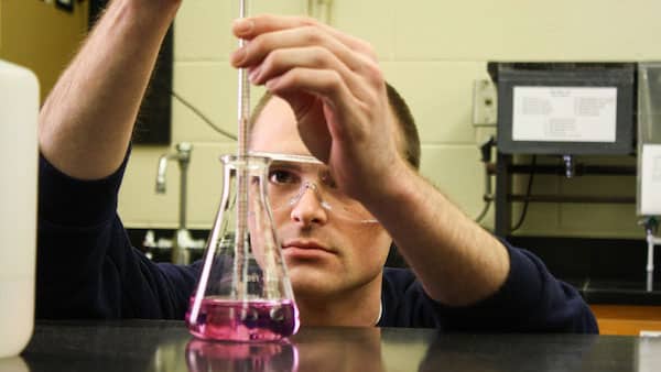 Luke Bessmer measuring out solution of pink liquid from a chemistry flask.