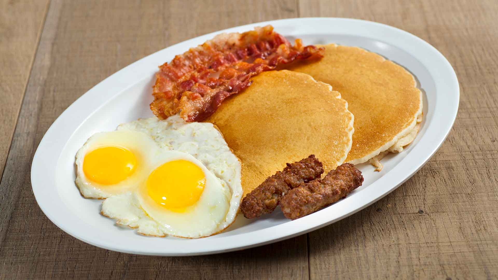 Breakfast platter of pancakes, eggs, bacon, and sausage.