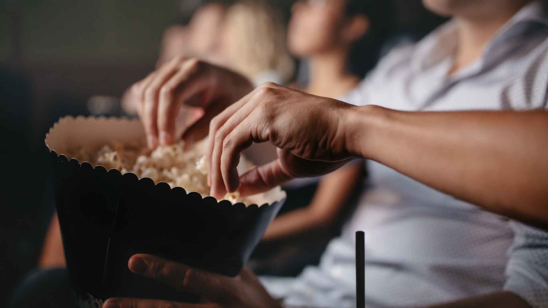 Several people eating popcorn in a movie theatre.