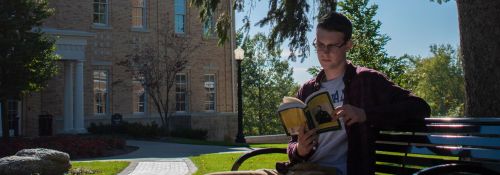 Student reading a book on a bench on campus.