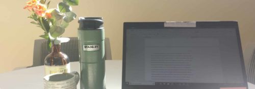 Thermos of tea and a laptop open for editing essays.