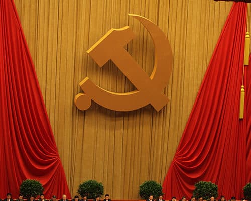 Rows of seated Chinese politicians with the Hammer and Sickle displayed on the back wall.