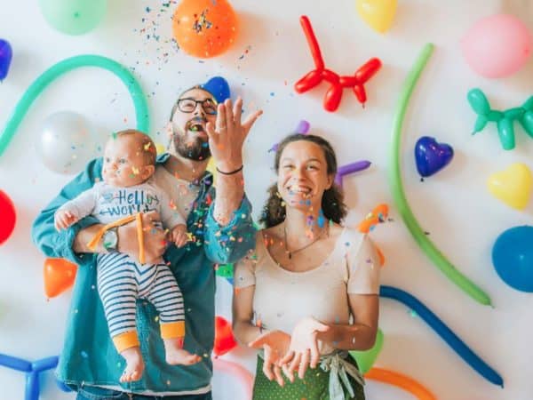Parents celebrate in front of a bright, colorful background of shaped balloons