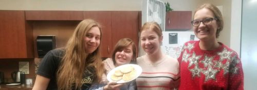 Four female students stand in a dorm kitchen with a plate of homemade tortillas