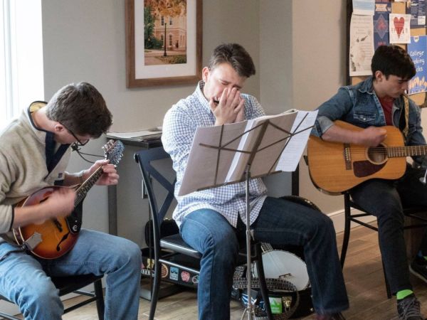 three male students sitting, playing acoustic music in a coffee house