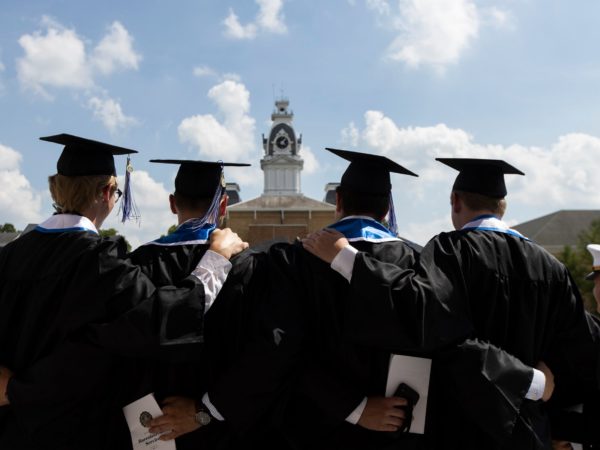 graduating students facing clocktower with blue skies