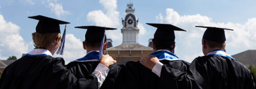 Four graduates in graduation robes look on at Central Hall